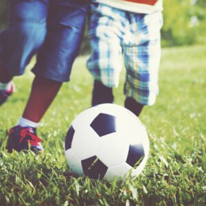 kids-playing-football-grass-min